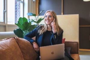 Women answering her phone with a laptop on her lap.